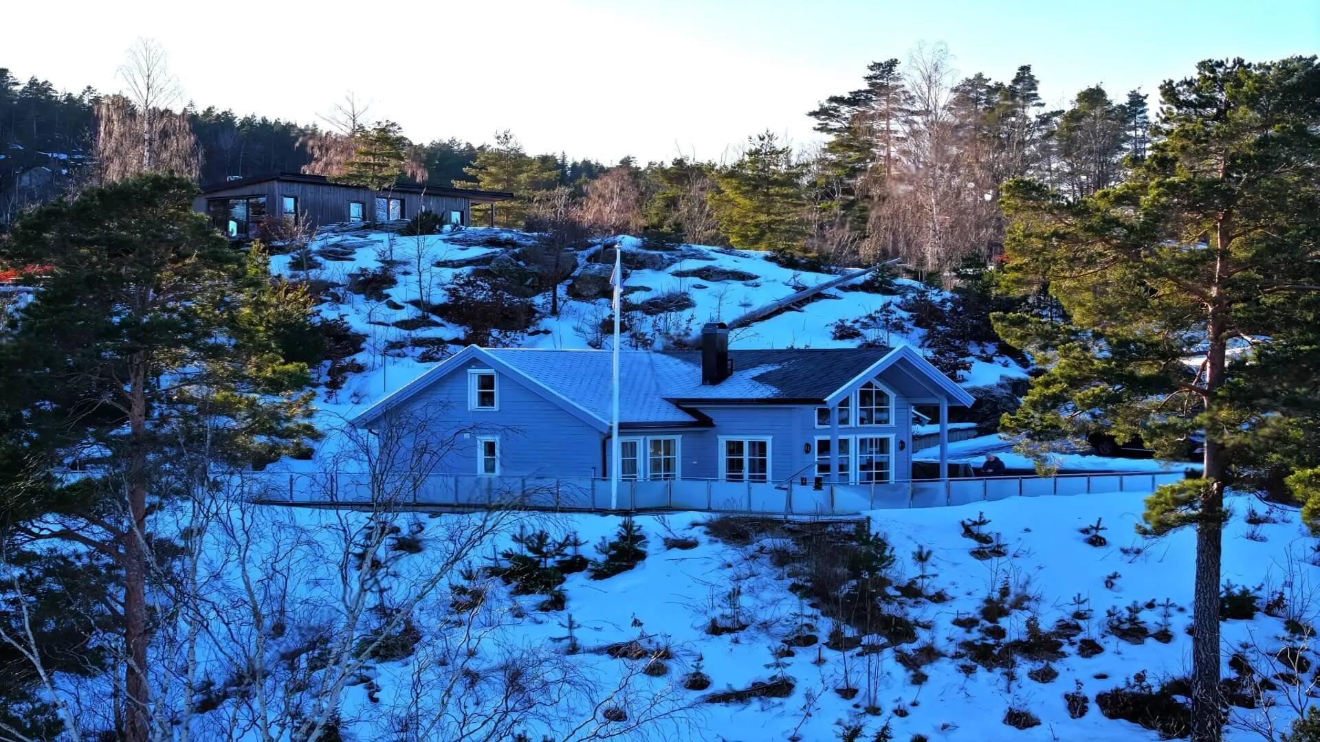 Dronefoto av hytter i snødekt terreng med skog rundt